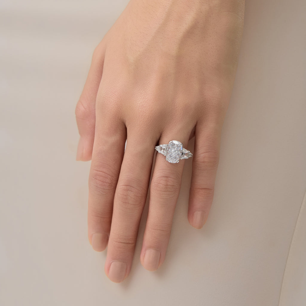 3.5 Carat Oval Multi-Stone Engagement Ring on finger touching a silk dress.