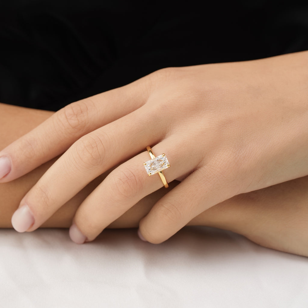 Gold ring with a diamond on a person's finger against a neutral background