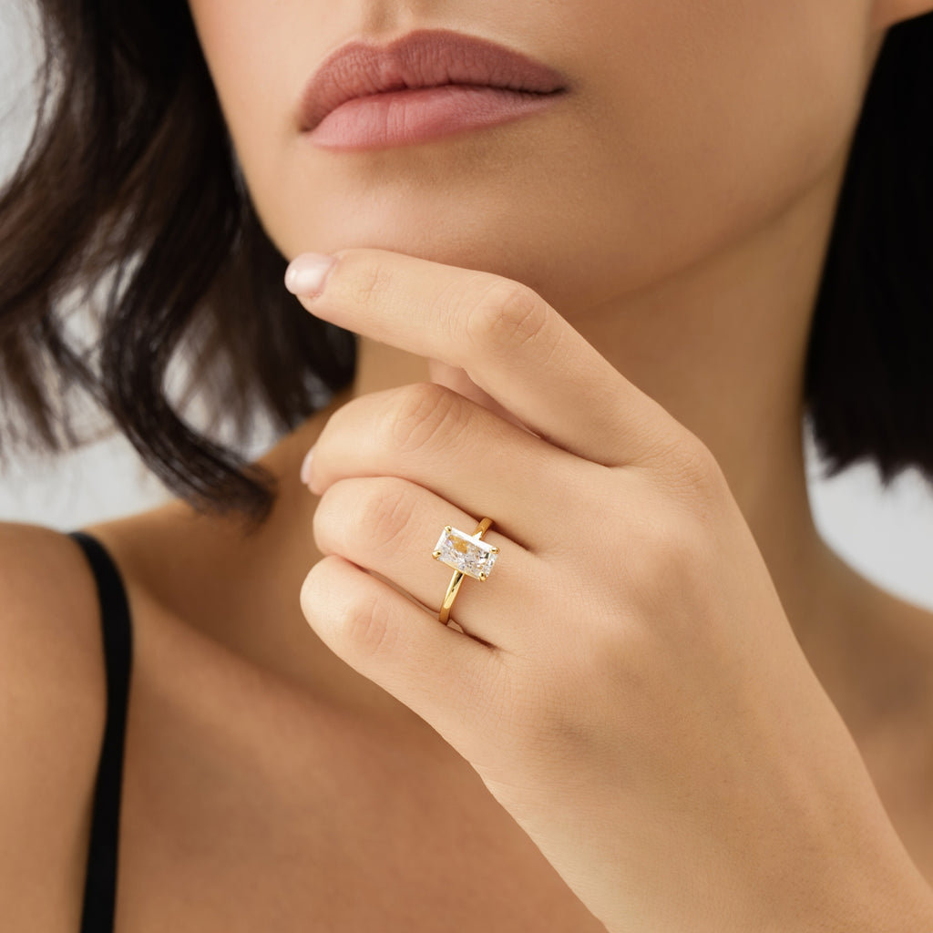 Close-up of a woman's hand wearing a gold ring with a diamond, touching her chin.