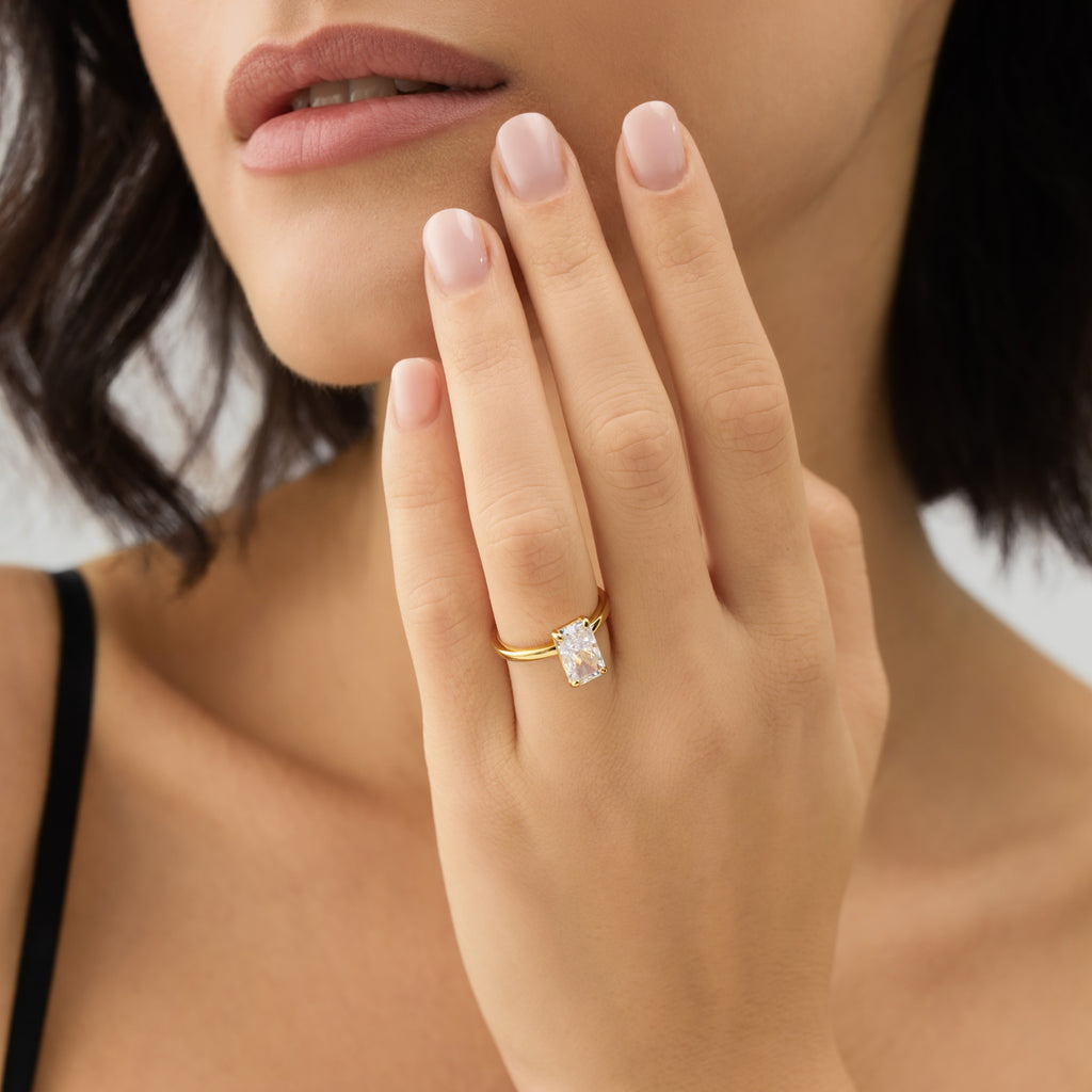 Close-up of a hand wearing a gold ring with a diamond, held near the face.