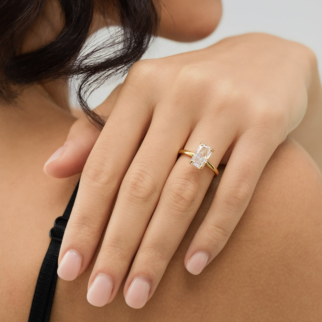 Close-up of a hand wearing a gold ring with a diamond on a neutral background