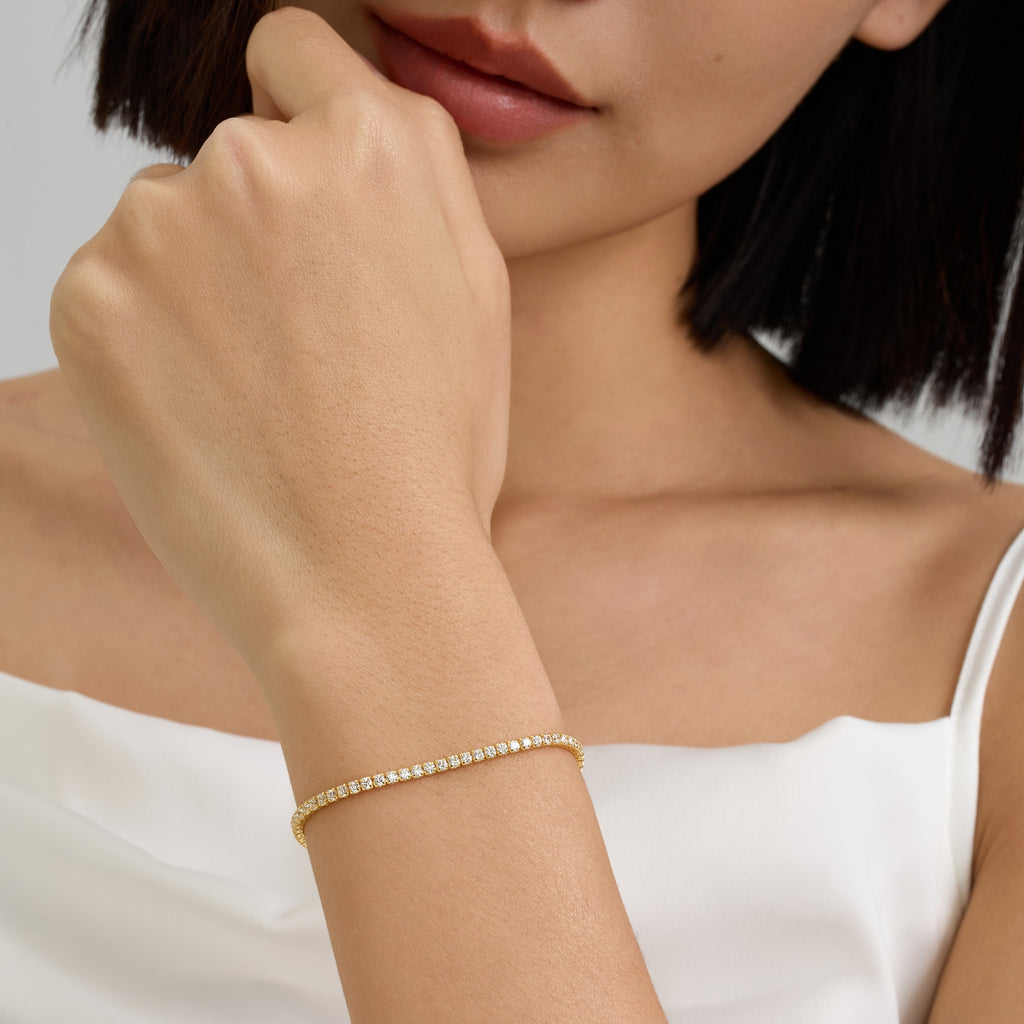 Woman Wearing 2mm Round Brilliant Tennis Bracelet in 18k Gold-Plated Sterling Silver with Diamond-Look Stones.