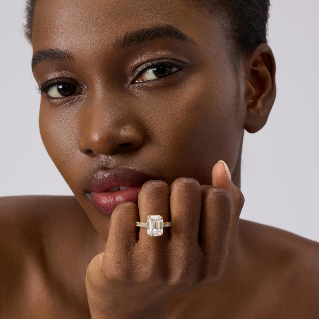 Club Lux 5ct emerald cut engagement ring worn by a lady, close-up front view, hidden halo, double prong, gold band