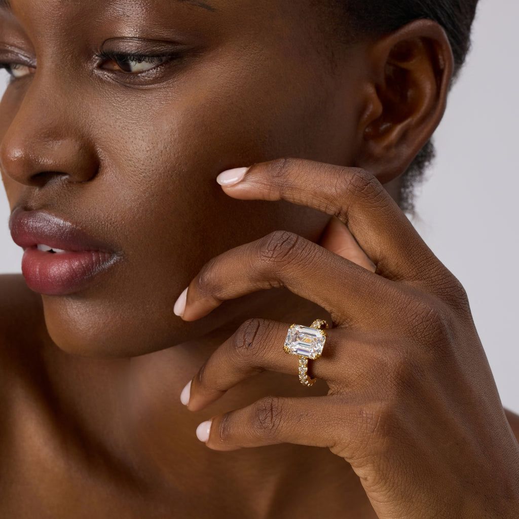 Club Lux 5ct emerald cut engagement ring on a lady's hand, slight angle front, hidden halo, double prong, gold band