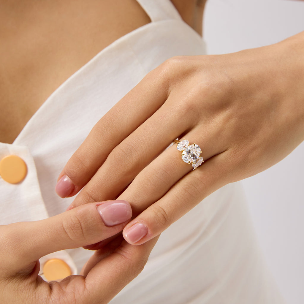 Front view of gold oval engagement ring as hand gently touches another hand.