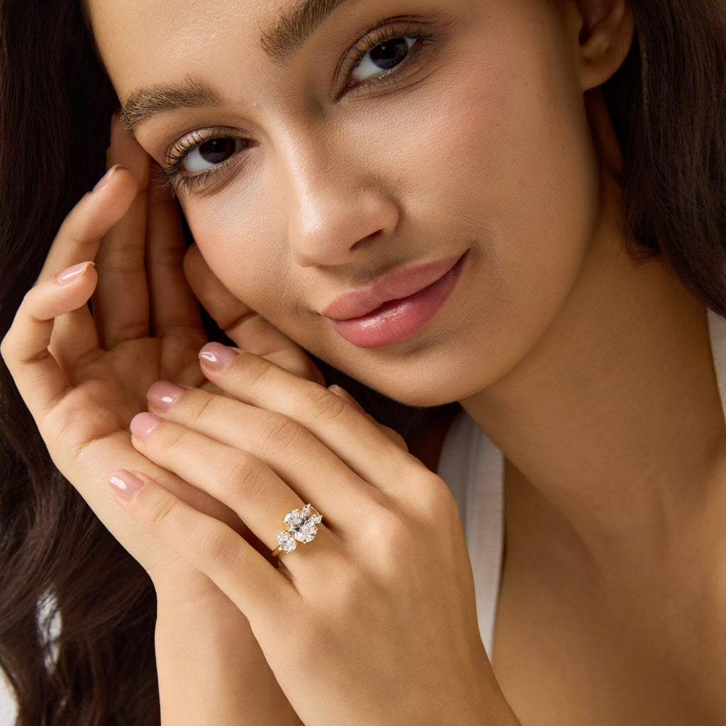 Close-up of woman wearing oval three-stone engagement ring, front and slight side angle.