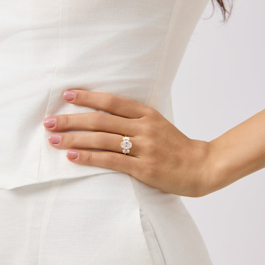 Hand wearing gold oval three stone ring with white dress background.