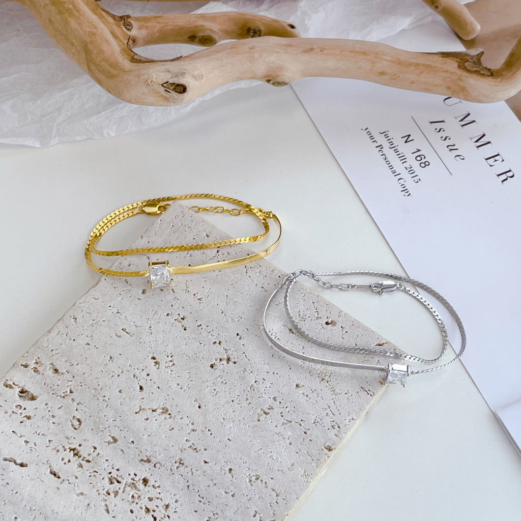 This statement bracelet is the layering must-have for fashionistas!  Crafted in sterling silver, a single rectangle-cut cubic zirconia's happily housed between two rows of flat snake chain and a sleek curved bar. Get it in glowing Gold or shining Silver Bracelet - the choice is yours!